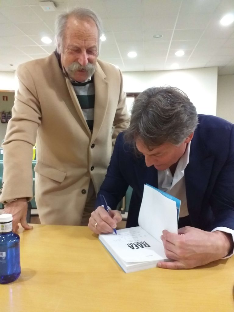 Rafa Pascual firma un ejemplar de su libro bajo la mirada de Ricardo Pérez y Verdes, del museo MELGA