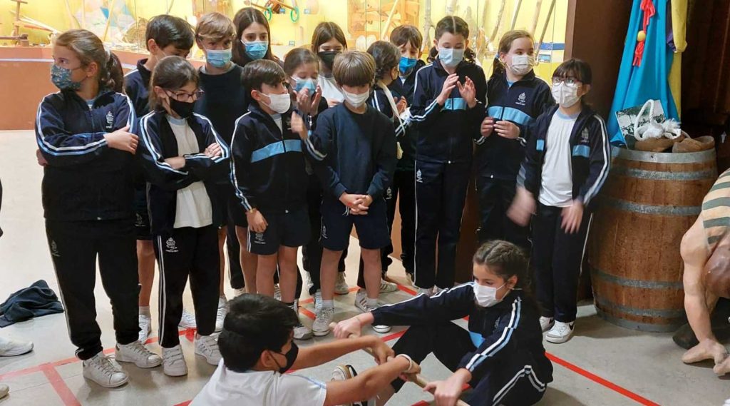 Un grupo de alumnos del colegio hijas de cristo rey observan como dos compañeros compiten con palo, juego tradicional, en el museo melga de ponteceso