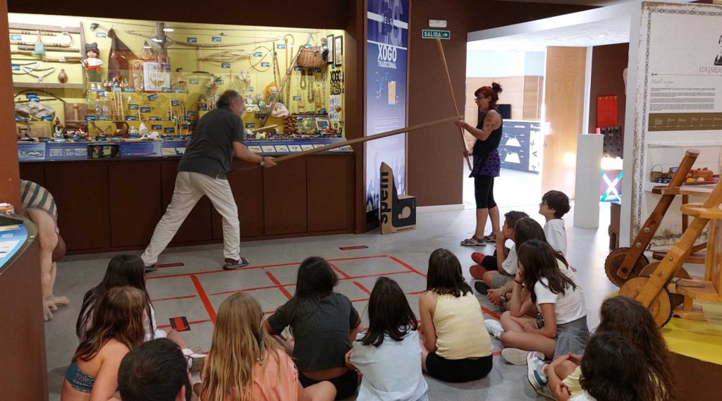 Ricardo Pérez y Verdes, presidente del Museo Melga de Ponteceso hace una demostración de un juego tradicional con una monitora, ante la atenta mirada de todos los jóvenes