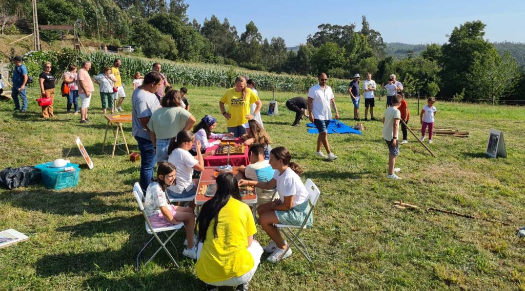 participantes de las noches del medievo de riobó sentados en mesas y sillas de camping y otros juegan, de fondo, a juegos medievales