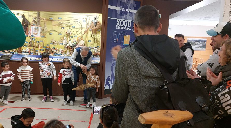 Varios niños miran como Ricardo Pérez y Verdes enseña a una pequeña niña a jugar a un juego tradicional en el museo melga ante la atenta mirada de los padres del grupo